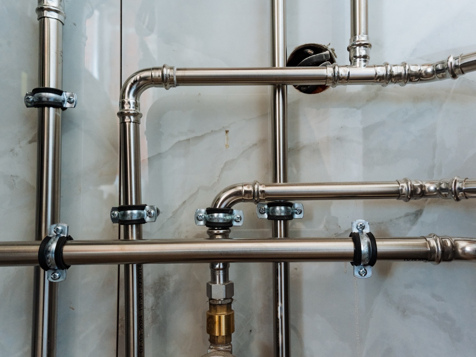 Stainless press-fit pipework clipped to a tiled wall, mid-install.