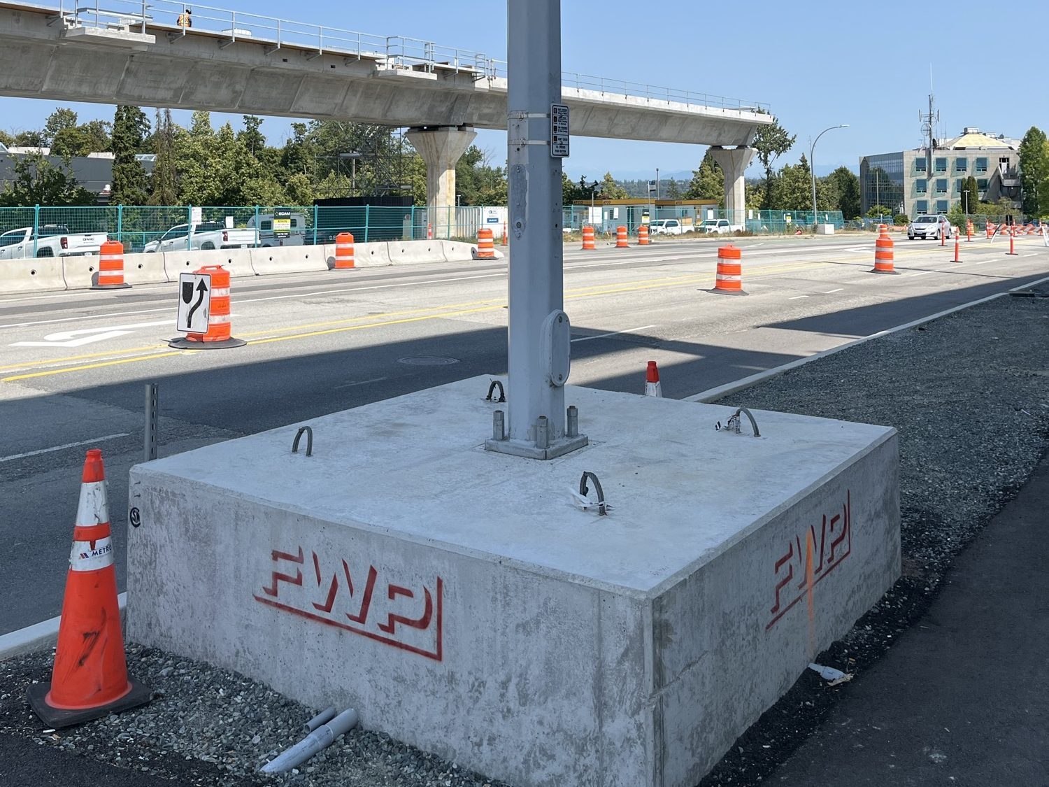 A traffic-signal pole standing on a Fraserway Prekast concrete base beside a new road