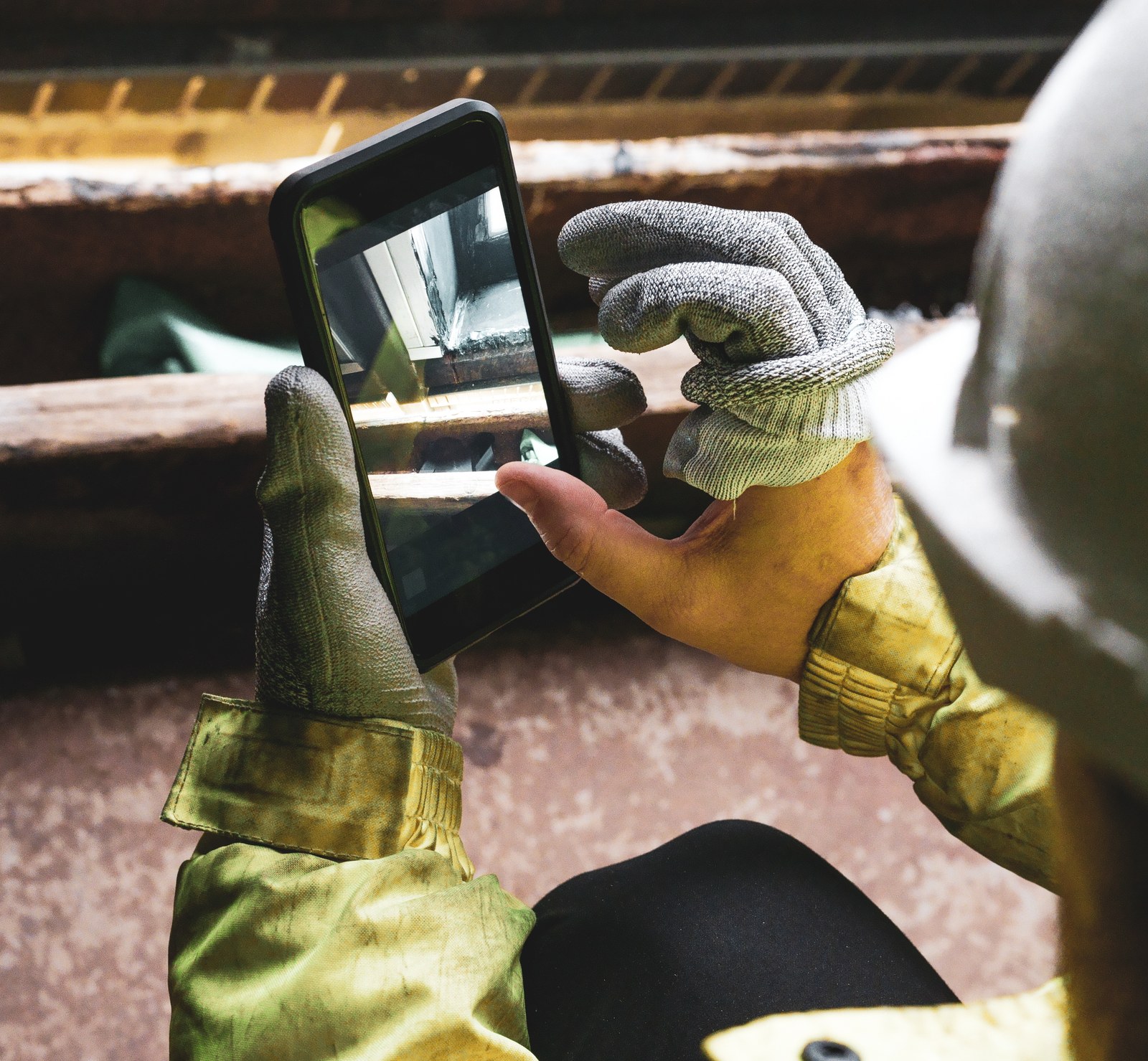 A gloved hand holding a phone at the work face, photographing the check as it happens